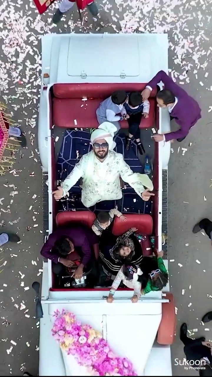 Groom celebrating with family in an open-top vintage-style car during his baraat