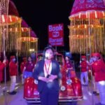 Book My Baraat coordinator standing in front of a red vintage-style car and illuminated baraat umbrellas