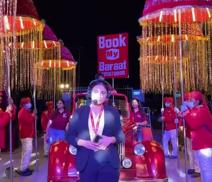 Book My Baraat coordinator standing in front of a red vintage-style car and illuminated baraat umbrellas