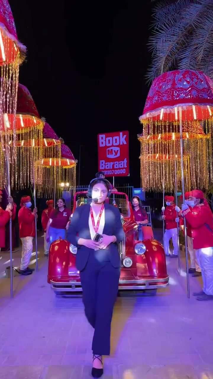 Book My Baraat coordinator standing in front of a red vintage-style car and illuminated baraat umbrellas
